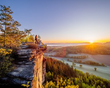 Dalmatiner und Frauchen auf einem Felsvorsprung bei Sonnenaufgang in der Sächsischen Schweiz