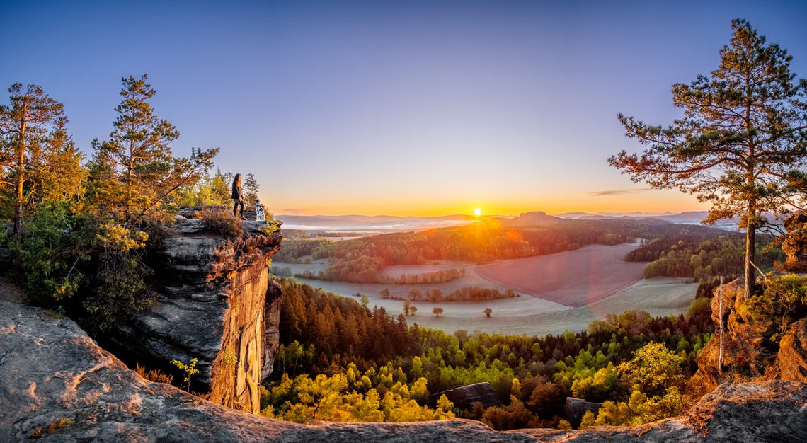 Dalmatiner und Frauchen auf einem Felsvorsprung bei Sonnenaufgang in der Sächsischen Schweiz