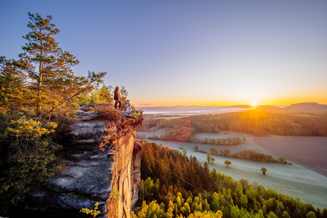 Dalmatiner und Frauchen auf einem Felsvorsprung bei Sonnenaufgang in der Sächsischen Schweiz