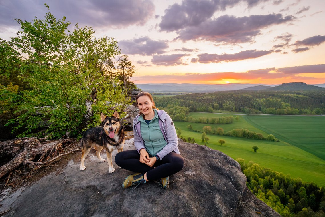 Hund und Frauchen sitzen im Morgenlicht auf einem Felsen