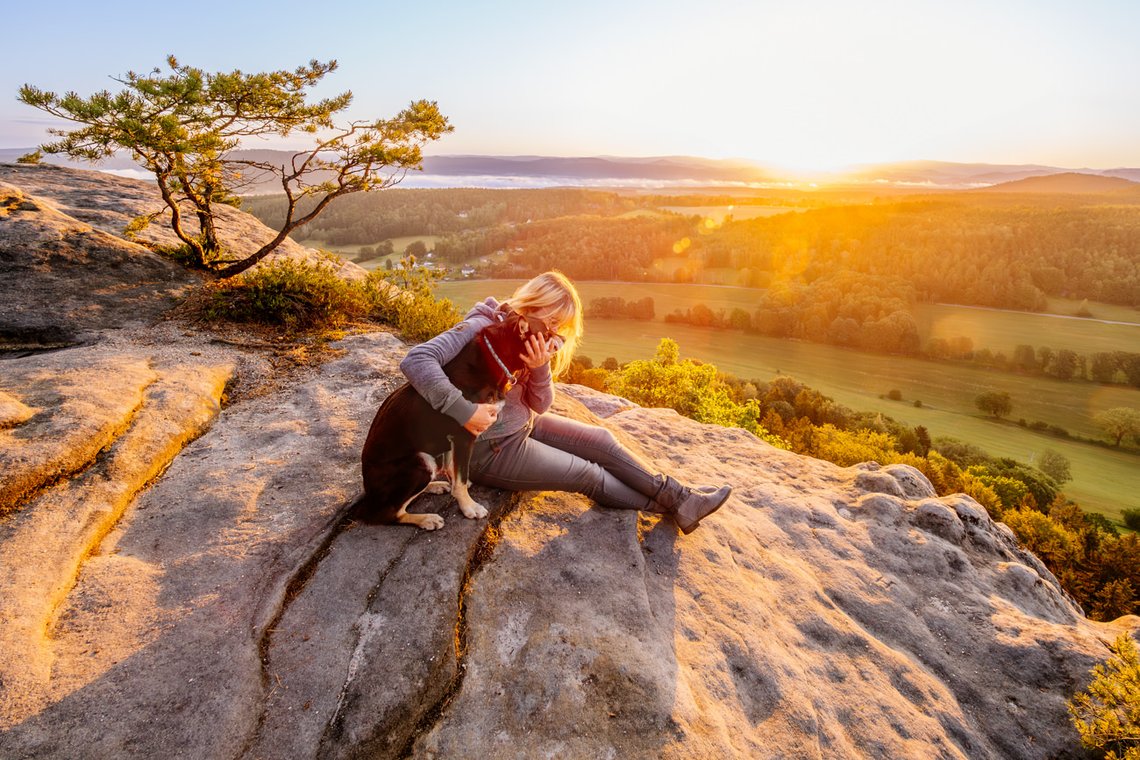 Mensch und Hund kuscheln im Sonnenaufgang in den Bergen